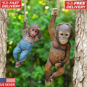 May include: Two realistic-looking monkey figurines hanging from ropes. The monkey on the left is wearing blue overalls and has brown fur. The monkey on the right is brown and has a more orangutan-like appearance.