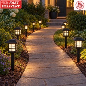 May include: A series of black solar-powered path lights with square, grid-patterned glass shades lining a stone walkway. Each light features a warm, glowing internal bulb, mounted on a black stake, illuminating the garden path at night.