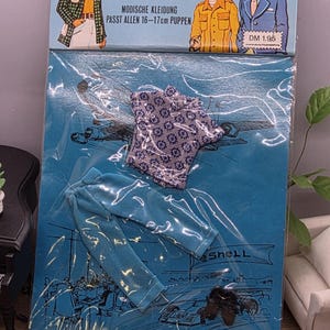 May include: Vintage doll clothing set in original packaging. The set includes a patterned shirt and blue pants. The packaging features illustrations of men's fashion and the word "Papa".
