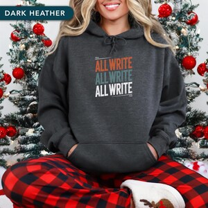 May include: Dark heather gray hoodie with the text "ALL WRITE ALL WRITE ALL WRITE" in orange, teal, and white. The hoodie has a drawstring hood and a front pocket. The image is set against a festive Christmas background.