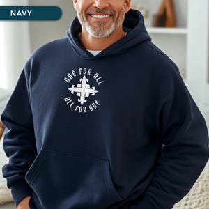 Peut inclure: Un sweat à capuche bleu marine avec un motif blanc représentant une croix et le texte "ONE FOR ALL, ALL FOR ONE". Le sweat à capuche a une capuche et une poche avant. Le mot "NAVY" est dans une bannière en haut à gauche.
