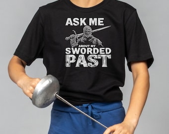 May include: Black t-shirt with a white graphic of a person in armor holding a sword. The text on the shirt reads "Ask me about my sworded past".