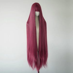 May include: A long, burgundy-colored wig with a blunt fringe. The wig is displayed on a mannequin head against a white background. The hair is straight and extends well past the shoulders.