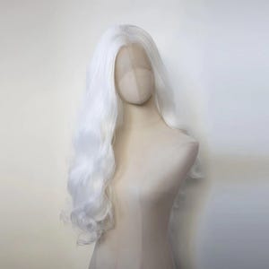 Könnte beinhalten: Eine lange, weiße Perücke mit lockeren Wellen. Die Perücke ist auf einem Mannequin-Kopf gestylt.
