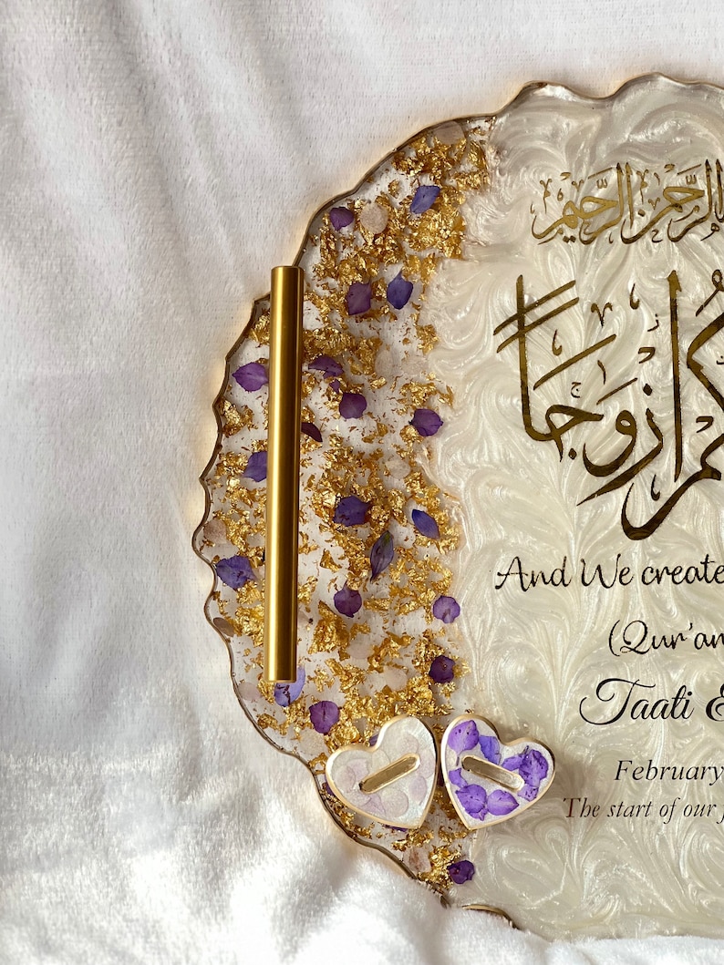 May include: A decorative resin tray with gold leaf accents, purple flower petals, and gold calligraphy. The tray has a wavy edge and includes two heart-shaped elements. Text on the tray reads "And We created you in pairs".