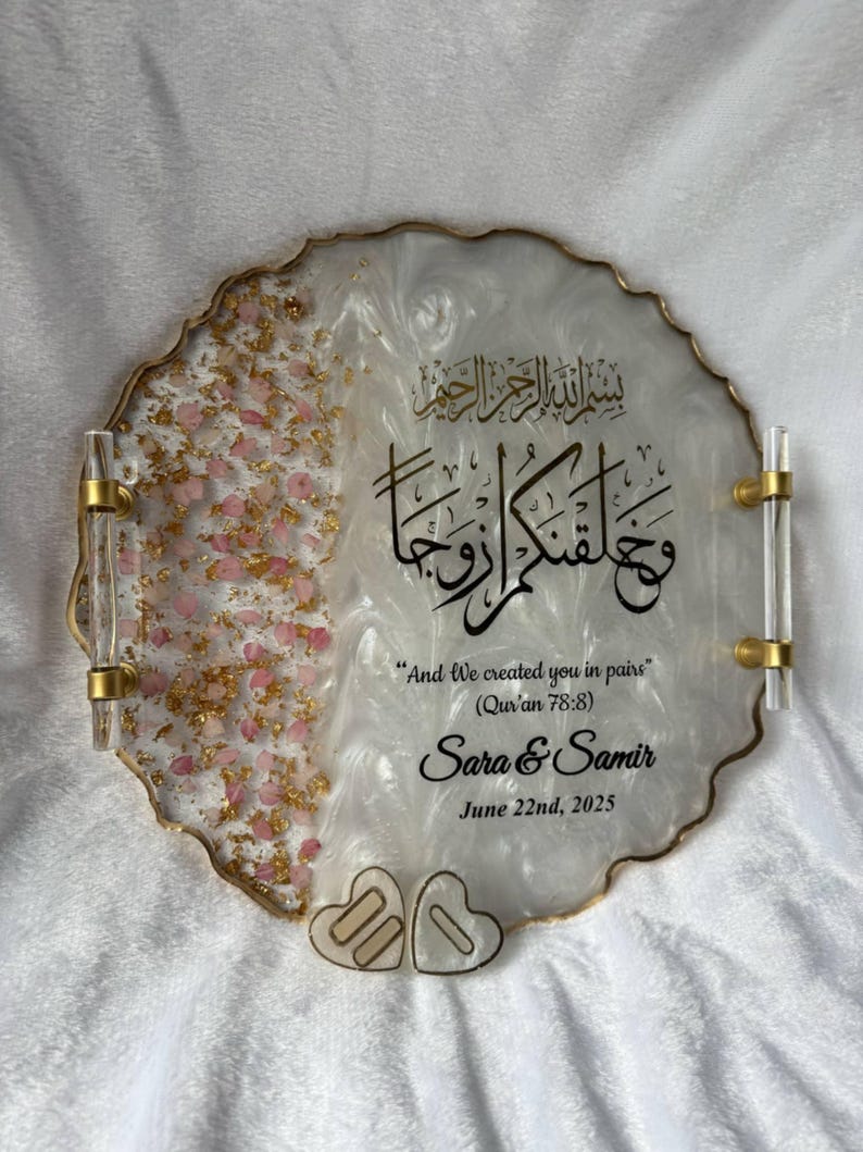 May include: A decorative tray with a white and gold design, featuring gold handles. The tray includes pink and gold accents, with Arabic calligraphy and the text "And We created you in pairs" and names "Sara & Samir" with a date.