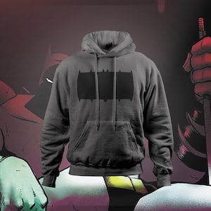 Puede incluir: Una sudadera con capucha gris carbón con el logotipo de Batman negro en el pecho. La sudadera con capucha tiene un bolsillo delantero y cordones. El fondo presenta ilustraciones de estilo cómic con una combinación de colores rojo y negro.