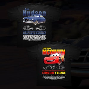 Puede incluir: Camiseta negra con una imagen de dibujos animados de Doc Hudson y Rayo McQueen de la franquicia de películas Cars. El texto en la camiseta dice "Doc Hudson, no soy un corredor elegante, pero estoy orgulloso de lo que soy. Flotar como un Cadillac" y "Rayo McQueen, Picar como un BMW".