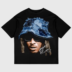 Könnte beinhalten: Schwarzes T-Shirt mit einem Aufdruck einer Person, die einen blauen Jeans-Bucket-Hut und eine Sonnenbrille trägt. Die Unterschrift der Person, "Future Rito", ist in Weiß unten rechts auf dem Aufdruck geschrieben.