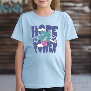 May include: Light blue t-shirt with a graphic design of a bird carrying a heart with the text "Hope is my super power" in blue and white.