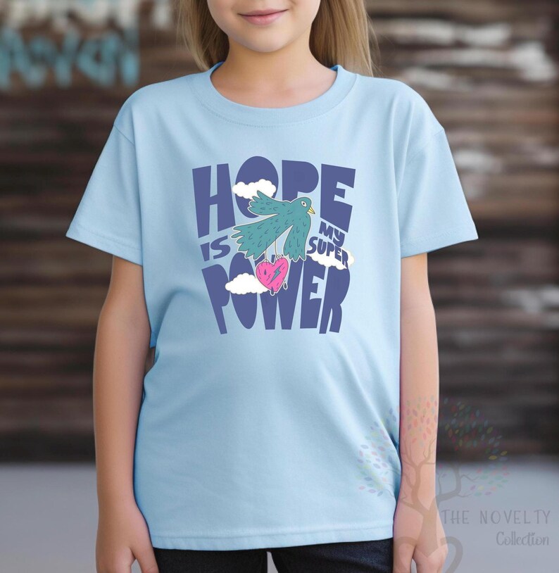 May include: Light blue t-shirt with a graphic design of a bird carrying a heart with the text "Hope is my super power" in blue and white.