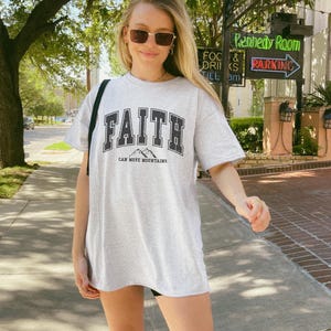 May include: An oversized grey t-shirt with a black graphic that says "FAITH CAN MOVE MOUNTAINS".