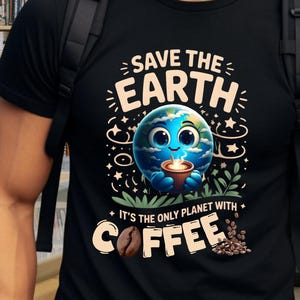 Op de afbeelding: Zwart T-shirt met de tekst "SAVE THE EARTH" en een afbeelding van de aarde met een koffiekopje. De tekst "IT'S THE ONLY PLANET WITH COFFEE" staat ook op het shirt. De afbeelding bevat koffiebonen.