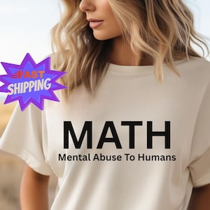 Peut inclure: Un t-shirt crème avec le mot "MATH" en lettres noires en gras, suivi de "Mental Abuse To Humans" en plus petit. Le t-shirt est porté par une personne aux cheveux bruns ondulés.
