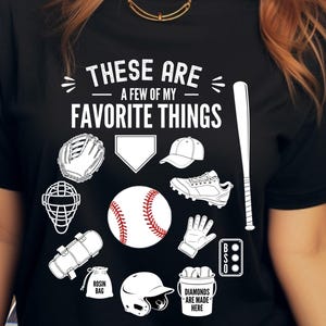 Op de afbeelding: Een zwart t-shirt met witte grafische illustraties van honkbaluitrusting, waaronder een handschoen, honkplaat, pet, knuppel, schoenplaatjes, catcher-masker, bal, slaghandschoen, harszakje, helm en een scorebord met de tekst DIAMONDS ARE MADE HERE.