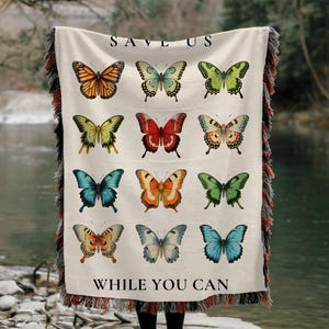 May include: A woven tapestry throw blanket with a white background and colorful butterfly illustrations. The text "Save Us While You Can" is printed in black at the bottom of the blanket.