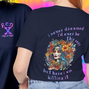 May include: Navy blue t-shirts with graphic designs. One shirt features "gen X" and the years 1965-1980. The other shirt displays a colorful illustration of a woman with floral accents and the text "i never dreamed i'd ever be this sexy but here i am killing it."
