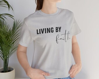 May include: A white t-shirt with black text that reads "LIVING BY faith".