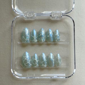 May include: A clear plastic case with ten light blue and white swirl-patterned false nails.