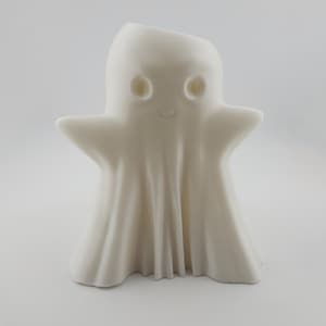 May include: A white ceramic ghost figure with a smiling face and outstretched arms. The ghost has a draped sheet-like appearance, with visible folds and a smooth texture. A Halloween or holiday decoration.