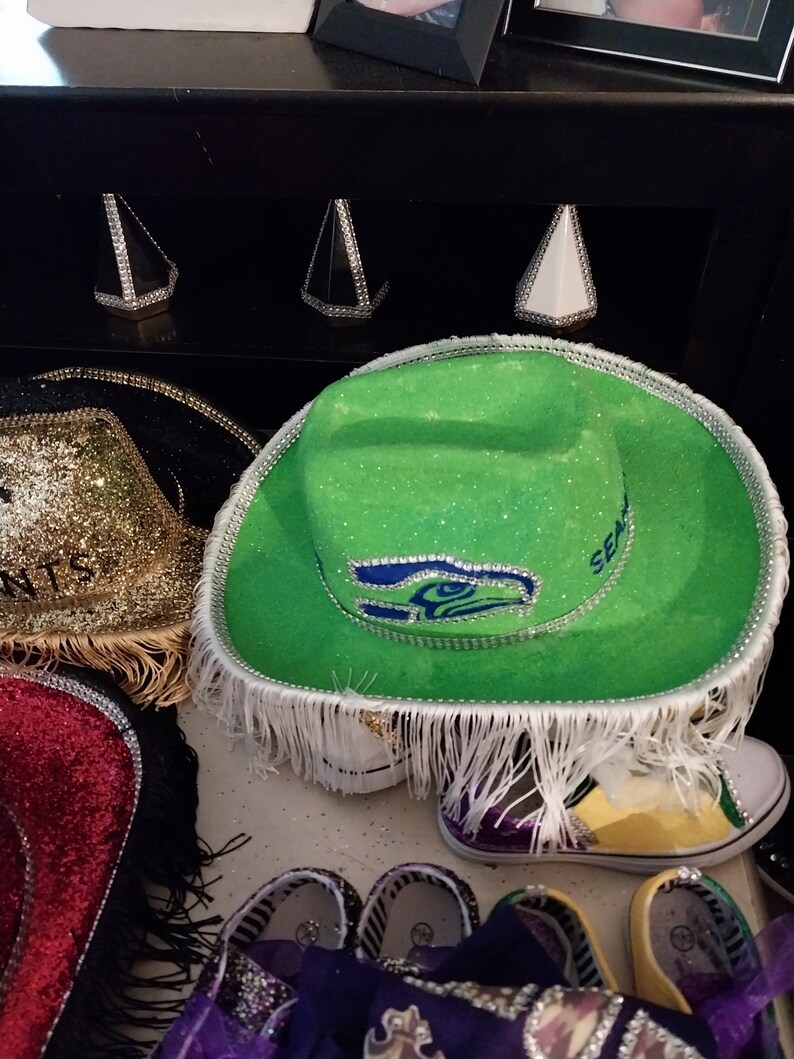 Może przedstawiać: Zielony i biały kapelusz kowbojski z logo Seattle Seahawks i kryształkami. Kapelusz ma biały frędzle wok&oacute;ł ronda.