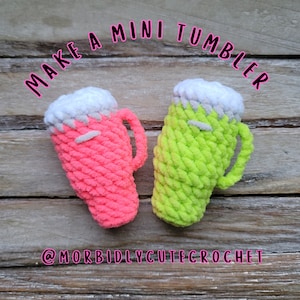 May include: Two crocheted mini tumblers, one pink and one green, with white crocheted foam on top. The tumblers are on a wooden surface with the text "MAKE A MINI TUMBLER" above them and "@MORBIDLYCUTECROCHET" below them.