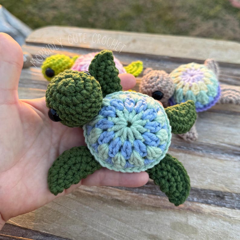 May include: A crocheted sea turtle with a green shell and a blue, green and white patterned shell. The turtle has black eyes and a small, green head.