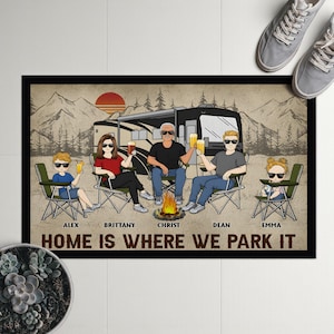 Könnte beinhalten: Rechteckige Fußmatte mit einer Familienillustration vor einem Wohnmobil und einem Lagerfeuer. Der Text "HOME IS WHERE WE PARK IT" wird unter den Namen der Familienmitglieder angezeigt: Alex, Brittany, Christ, Dean und Emma. Der Hintergrund zeigt Berge und einen Sonnenuntergang.