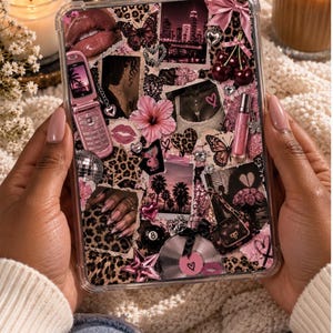 May include: A clear tablet case featuring a collage of pink and black imagery, including a flip phone, cherries, a disco ball, leopard print, butterflies, palm trees, a city skyline, and various heart-shaped accents on a rectangular surface.