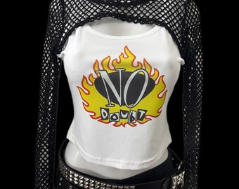 May include: A white crop top with the words "NO DOUBT" in a yellow and orange flame design. The top is paired with a black fishnet shrug and a studded belt, creating a layered, edgy look.