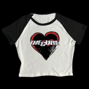 May include: White and black baseball tee shirt with a red heart and the text "THE CURE" in silver lettering.