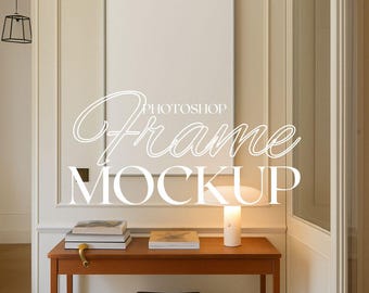 May include: A white frame mockup in a room with a wooden table, a lamp, and books. The frame is hanging on a white wall with white trim.