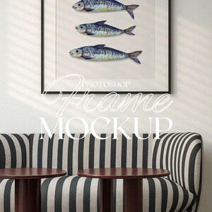 May include: A black framed picture with a white background and three watercolor illustrations of fish. The picture is hanging on a white wall above a black and white striped couch with two brown tables.