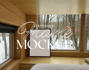 May include: A black picture frame mockup on a wooden shelf with a white bedspread in the foreground. The frame is sitting on a wooden shelf in front of a window with a view of a snowy forest.