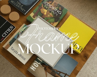 May include: A white picture frame mockup on a wooden table with various books and magazines. The frame is surrounded by books with titles like "Cooking in Spain", "Cities", and "Taryta Vilnius".