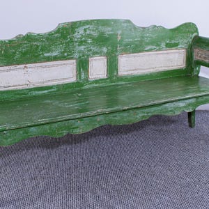 Può includere: Una panca in legno verde anticato con bordo del sedile e schienale smerlati. La panca ha uno schienale rettangolare con pannelli dipinti di bianco. La panca ha un aspetto usurato, che suggerisce età e utilizzo. È un mobile vintage.
