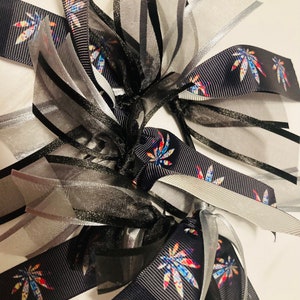 Könnte beinhalten: Nahaufnahme eines schwarzen und silbernen Bandes mit einem bunten Marihuana-Blatt-Muster. Das Band ist zu einer Schleife gebunden und bereit, zum Verpacken von Geschenken oder für andere dekorative Zwecke verwendet zu werden.