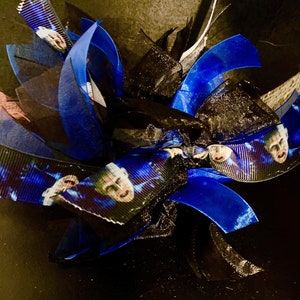 Könnte beinhalten: Eine blaue und schwarze Schleife mit einem gedruckten Bild eines Männergesichts. Die Schleife besteht aus Band und Tüll.