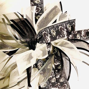May include: A decorative bow featuring a mix of black, white, and gray ribbons. Some ribbons have a repeating pattern with the text "LED ZEPPELIN" and images. The bow is layered with various textures and patterns.