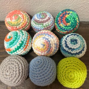 May include: Nine colorful, handmade crochet balls in various colors, including orange, green, blue, and gray. The balls are arranged in a grid pattern, showcasing the texture and spiral designs. These decorative balls are perfect for play or display.