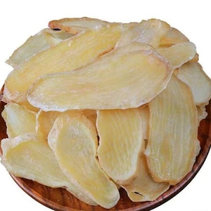 Puede incluir: Primer plano de un montón de rodajas de jengibre seco en un plato de madera. El jengibre es de color amarillo pálido y translúcido, con una textura ligeramente arrugada.