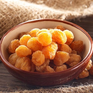 May include: A brown bowl filled with dried longan fruit. The fruit is light brown and has a slightly wrinkled texture.