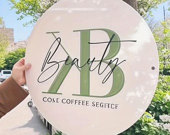 Op de afbeelding: Een ronde, witte plaat met het woord "Beauty" in cursief en de letters "KB" in groen. De plaat bevat ook de tekst "COSE COFFEE SEGITCE". De diameter van de plaat is 60 cm.