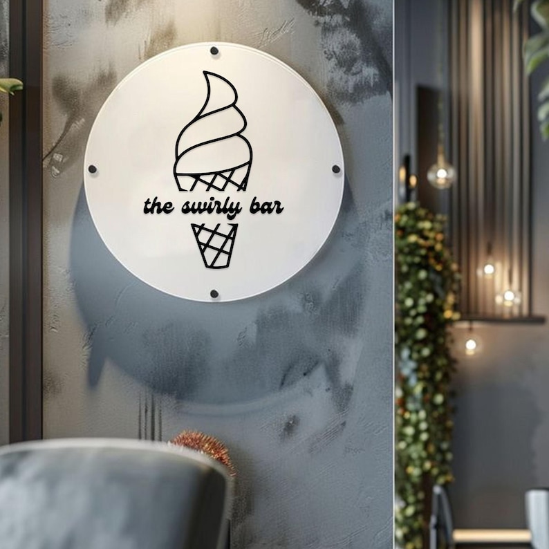May include: A circular white sign featuring the words "the swirly bar" and a black ice cream cone design. The sign is attached to a textured grey wall with small black fixings. It's likely a shop sign.