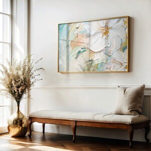 May include: A white, gold, and blue abstract painting in a gold frame hangs on a white wall above a wooden bench with a white cushion and a beige pillow. A gold vase with white flowers sits on the floor next to the bench.