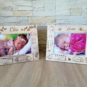 Peut inclure: Deux cadres photo en bois avec des détails gravés. Chaque cadre contient une photo de bébé. Un cadre porte le nom "Cléo" et la date "14 mars 2022". L'autre cadre porte le nom "Lana" et la date "07 novembre 2015".