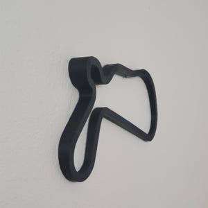May include: A black, abstract wall decoration in the shape of a stylized track layout. The design is mounted on a white wall, creating a contrast between the dark object and the light background. The piece has a modern, minimalist aesthetic.