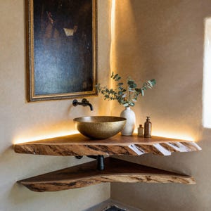 Puede incluir: Un tocador de baño rústico con una encimera de madera y un lavabo de latón. El tocador está iluminado con una luz cálida y ambiental. Un cuadro enmarcado cuelga de la pared detrás del lavabo.