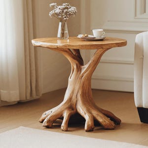May include: A round wooden side table with a tree trunk base and a natural wood finish. The table has a unique, organic shape and is perfect for adding a touch of nature to any room.