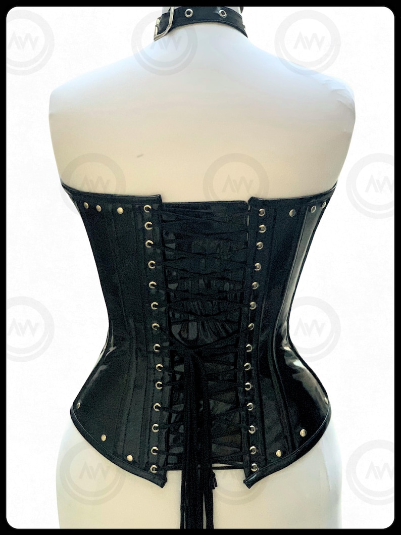 May include: Black corset with a matching choker. The corset features a glossy finish, metal eyelets, and a lace-up back. The choker has a buckle closure. The corset is displayed on a mannequin.